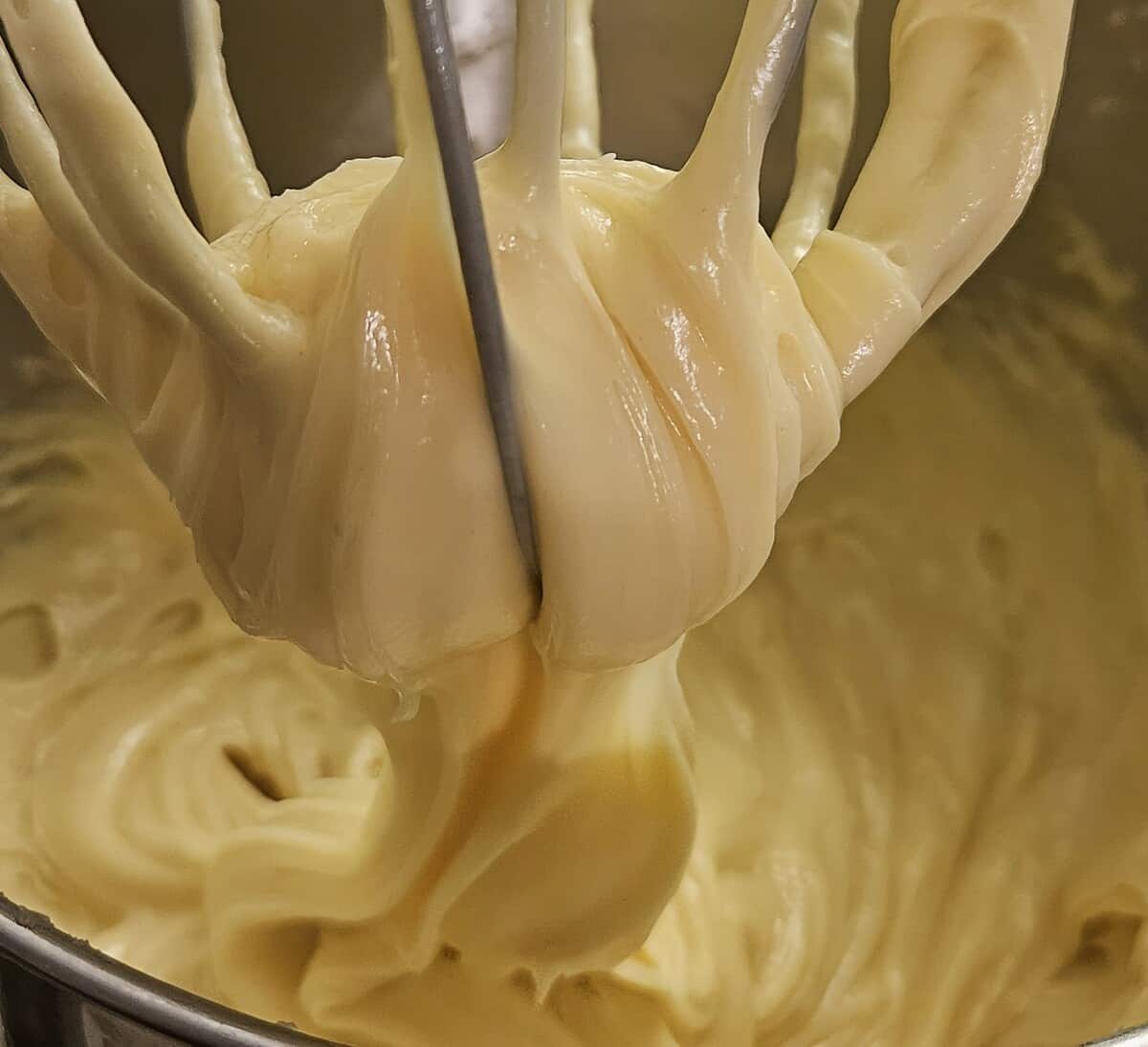 mixer whip attachment with finished pate choux batter flowing from it into the bowl, showing the smooth consistency.