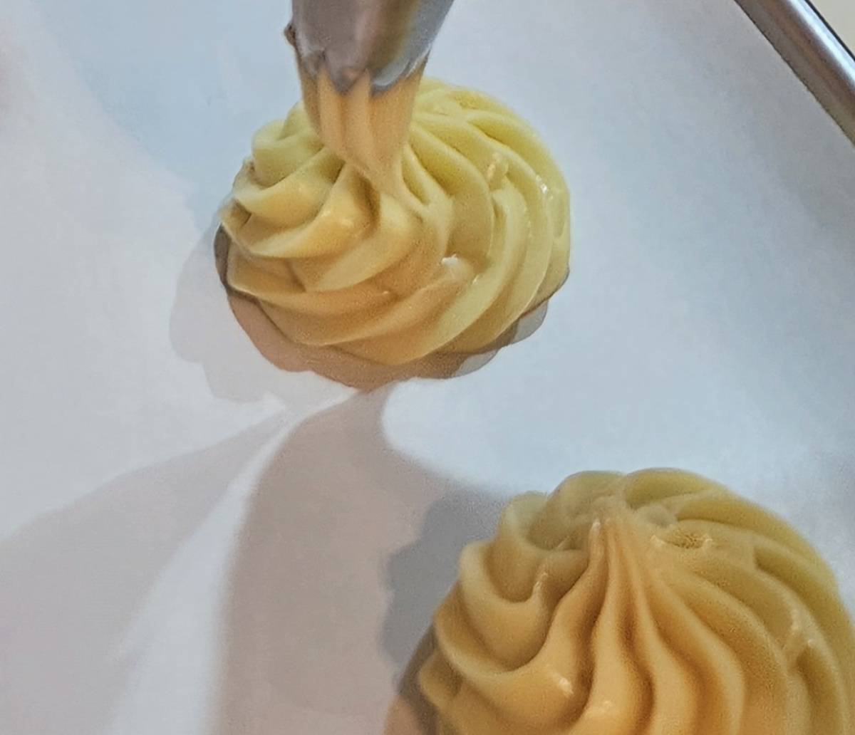 finished pate choux batter being piped onto a parchment lined sheet pan in a decorative rosette pattern.