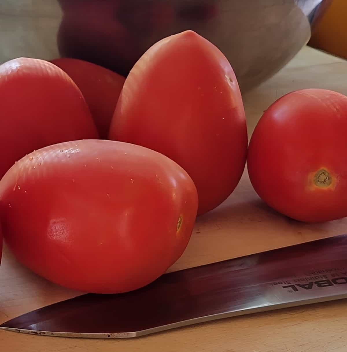 cutting board, knife, and whole tomatoes