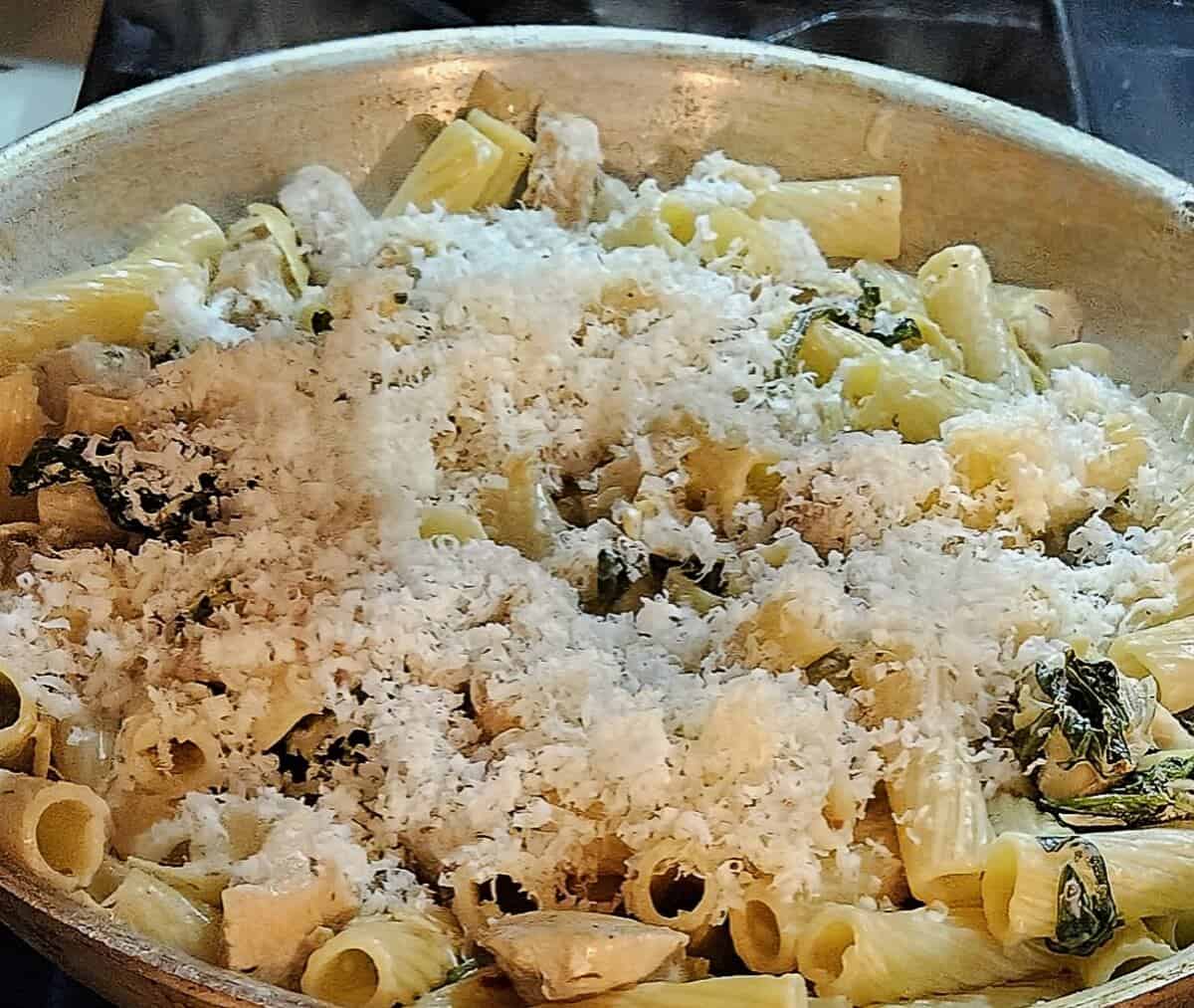 spinach and artichoke chicken pasta with finely grated asiago cheese on top in a skillet.