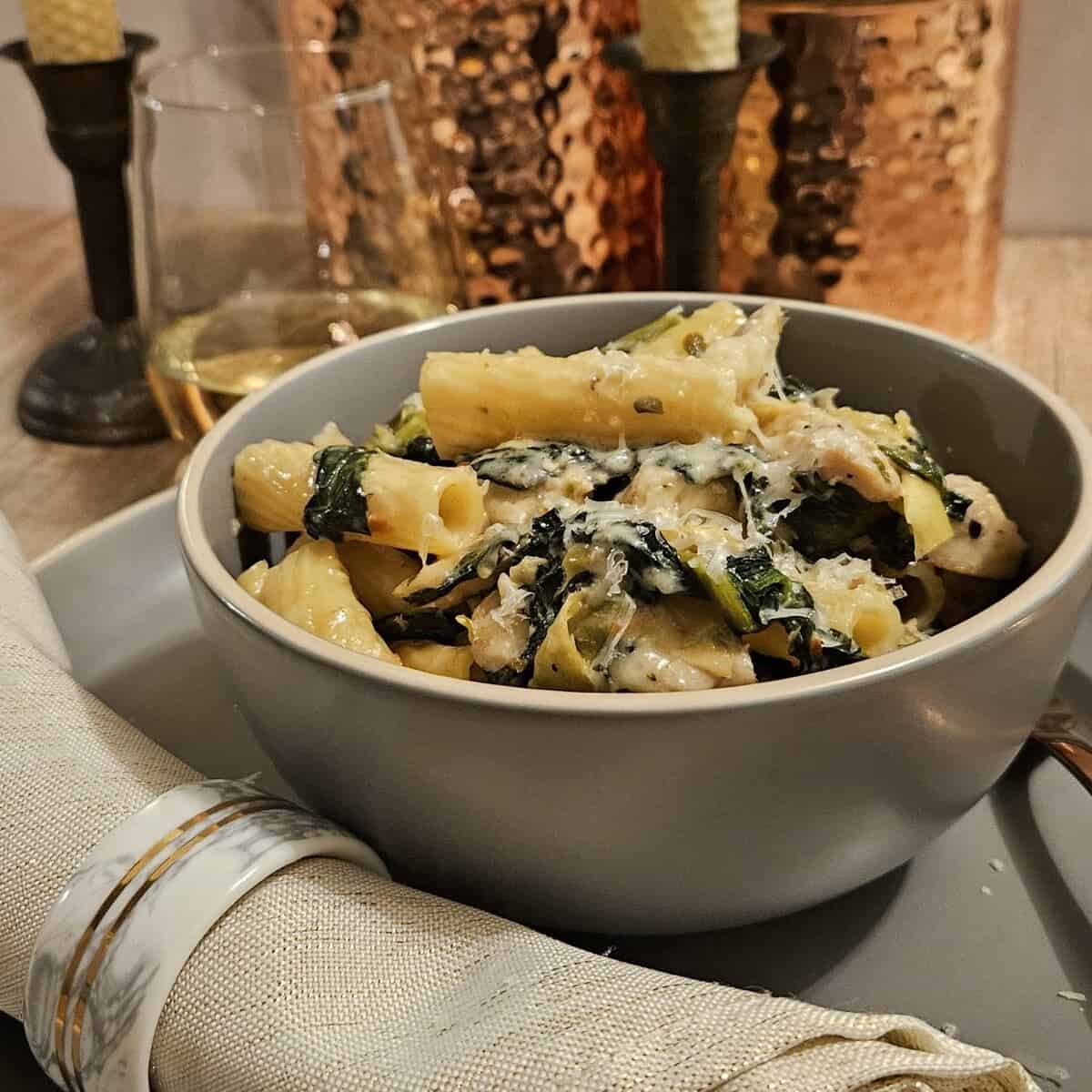 bowl of rigatoni pasta with spinach artichoke and chicken topped with parmesan cheese.