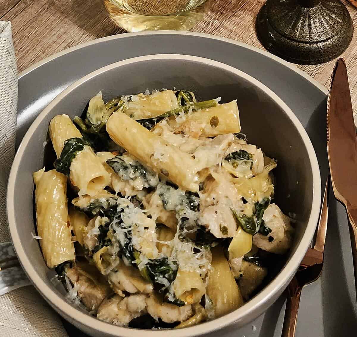 finished chicken, spinach and artichoke rigatoni pasta in a bowl, with grated asiago cheese on top.