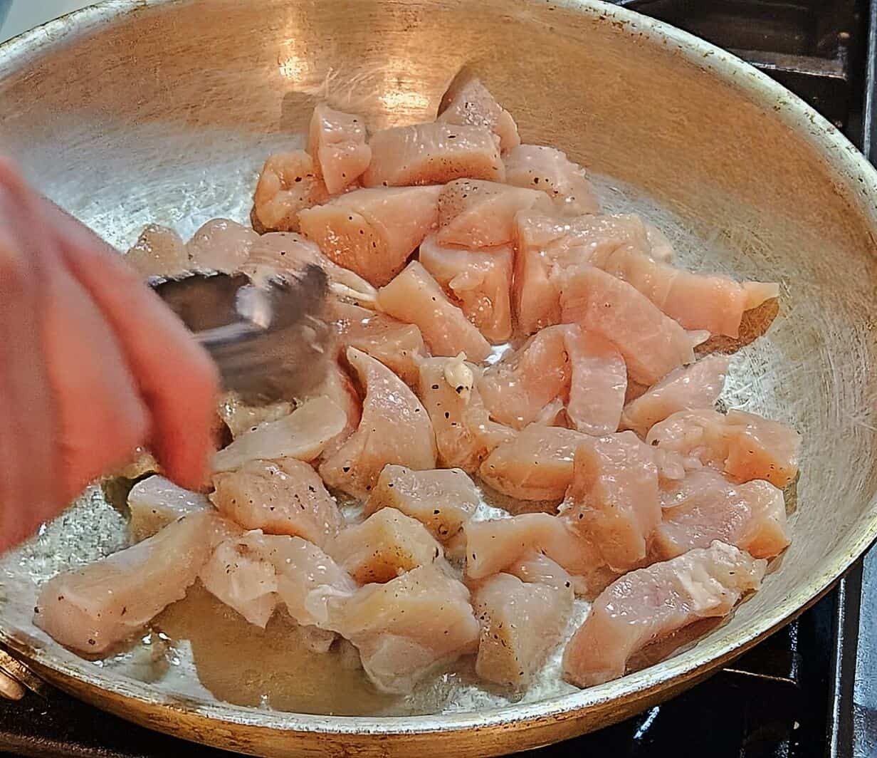 raw chicken breast pieces being seared in a skillet.