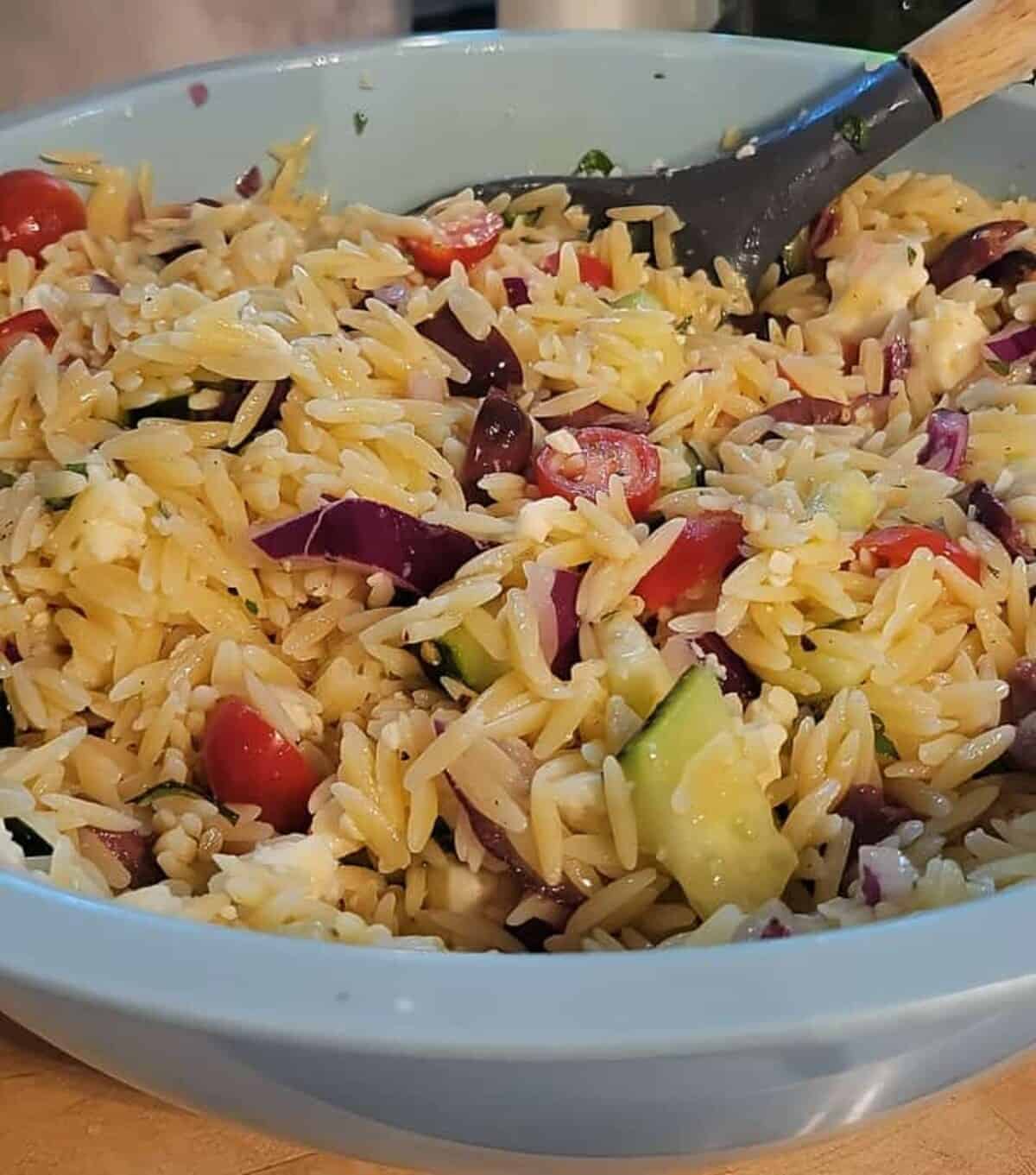 orzo salad being mixed together with a spoon in a mixing bowl.