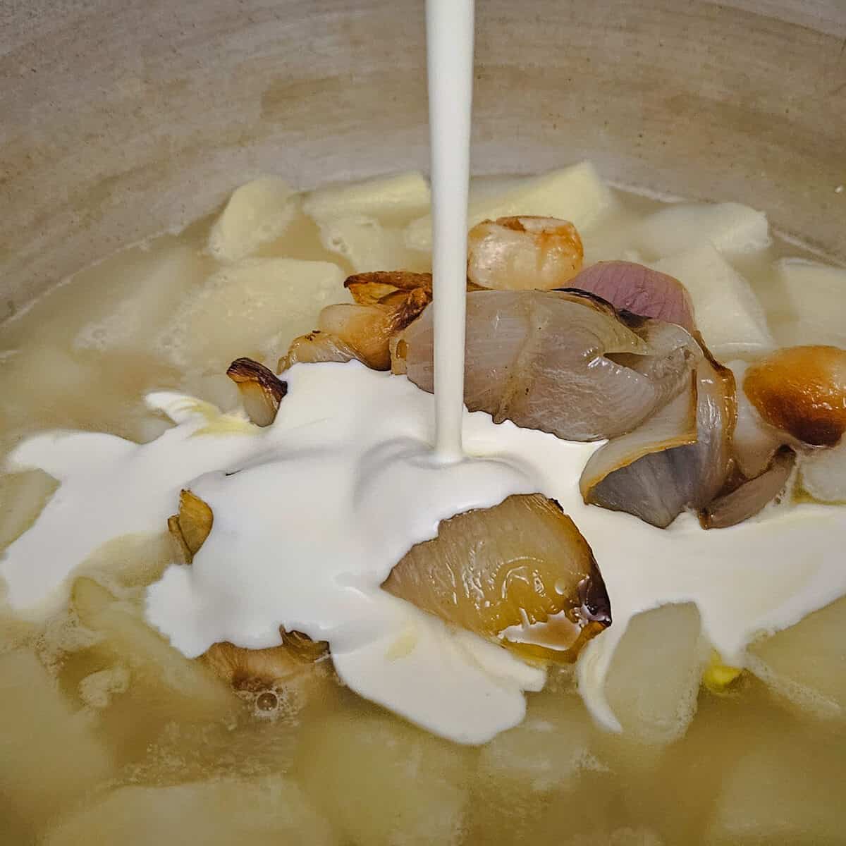 adding cream to the cooked potatoes and roasted shallots and garlic, for the potato and shallot soup with crispy prosciutto