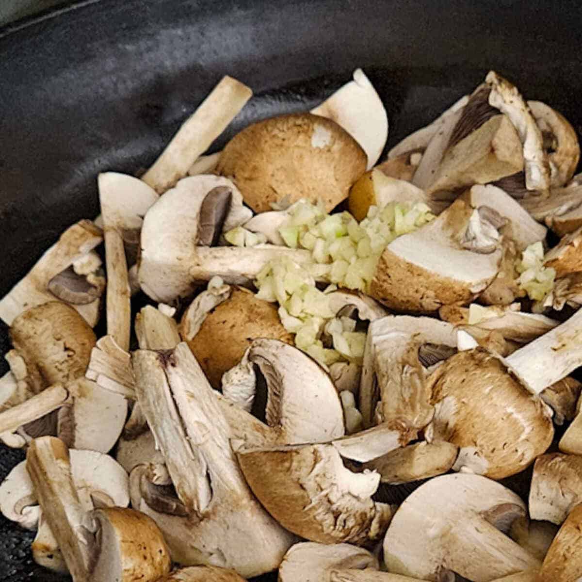adding chopped garlic to a pan of mushrooms cooking for the pasta carbonara with mushrooms