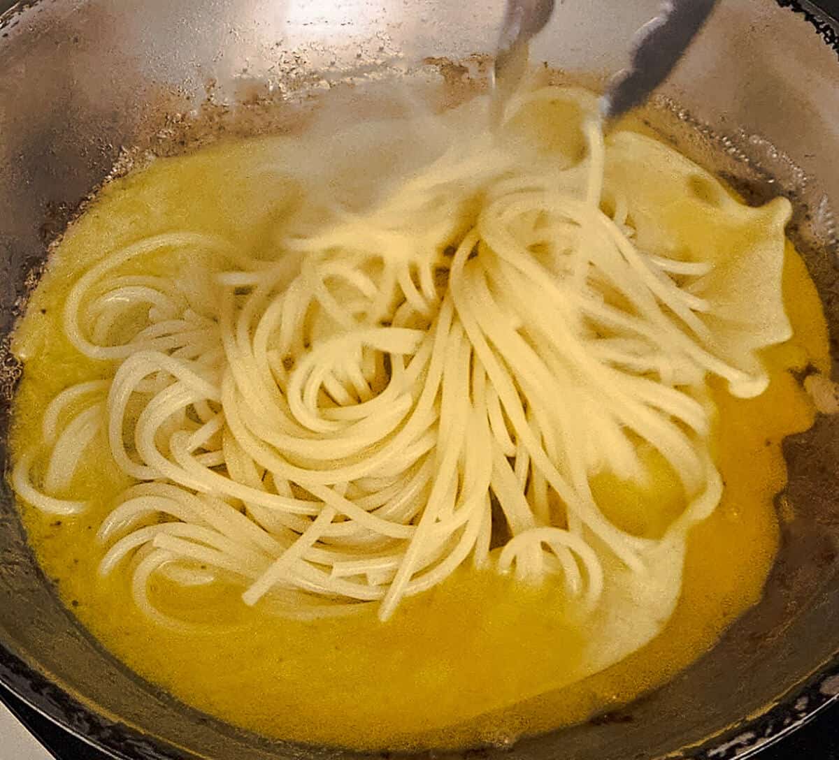 tossing the cooked pasta with the sauce in the pan for the pasta carbonara with mushrooms