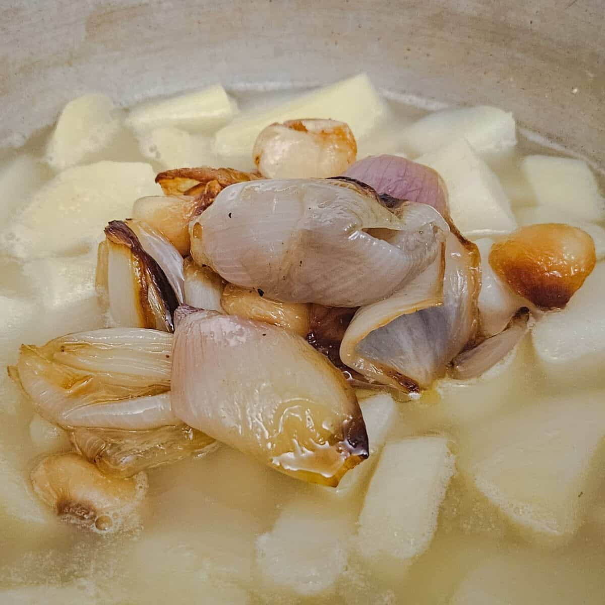 adding the roasted shallots and garlic to the cooked potatoes for the potato and shallot soup with crispy prosciutto