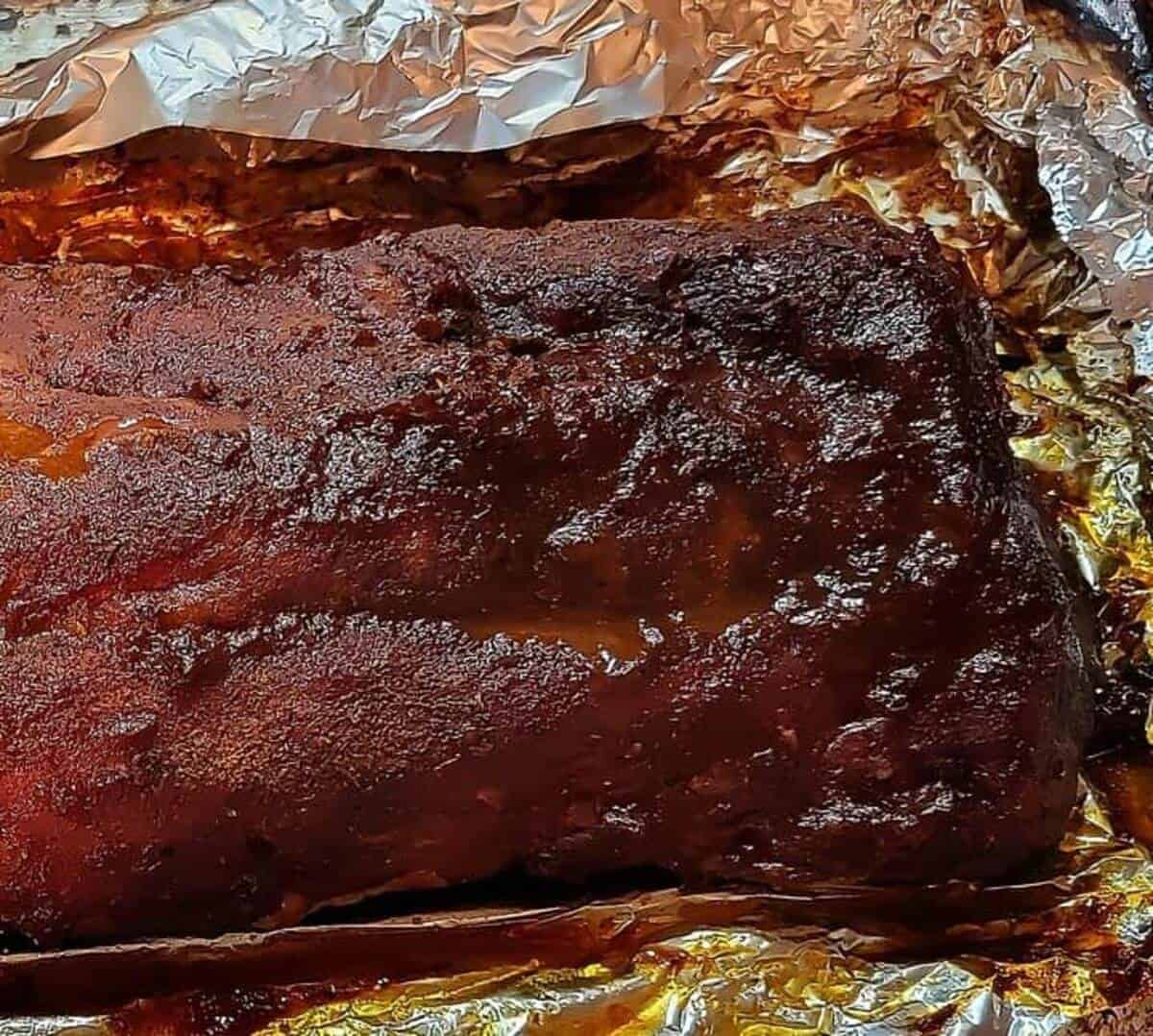 close up of finished rack of ribs, showing dark bronzed bark and juices, in open foil