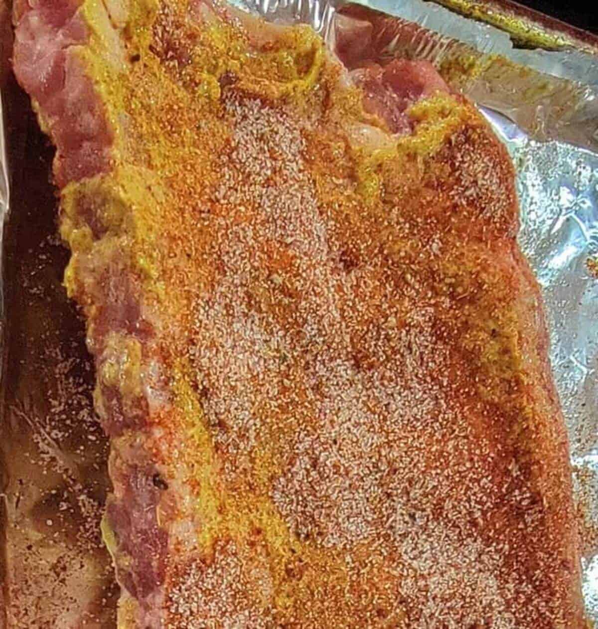 close up of back side of rib rack, covered in mustard and seasoning