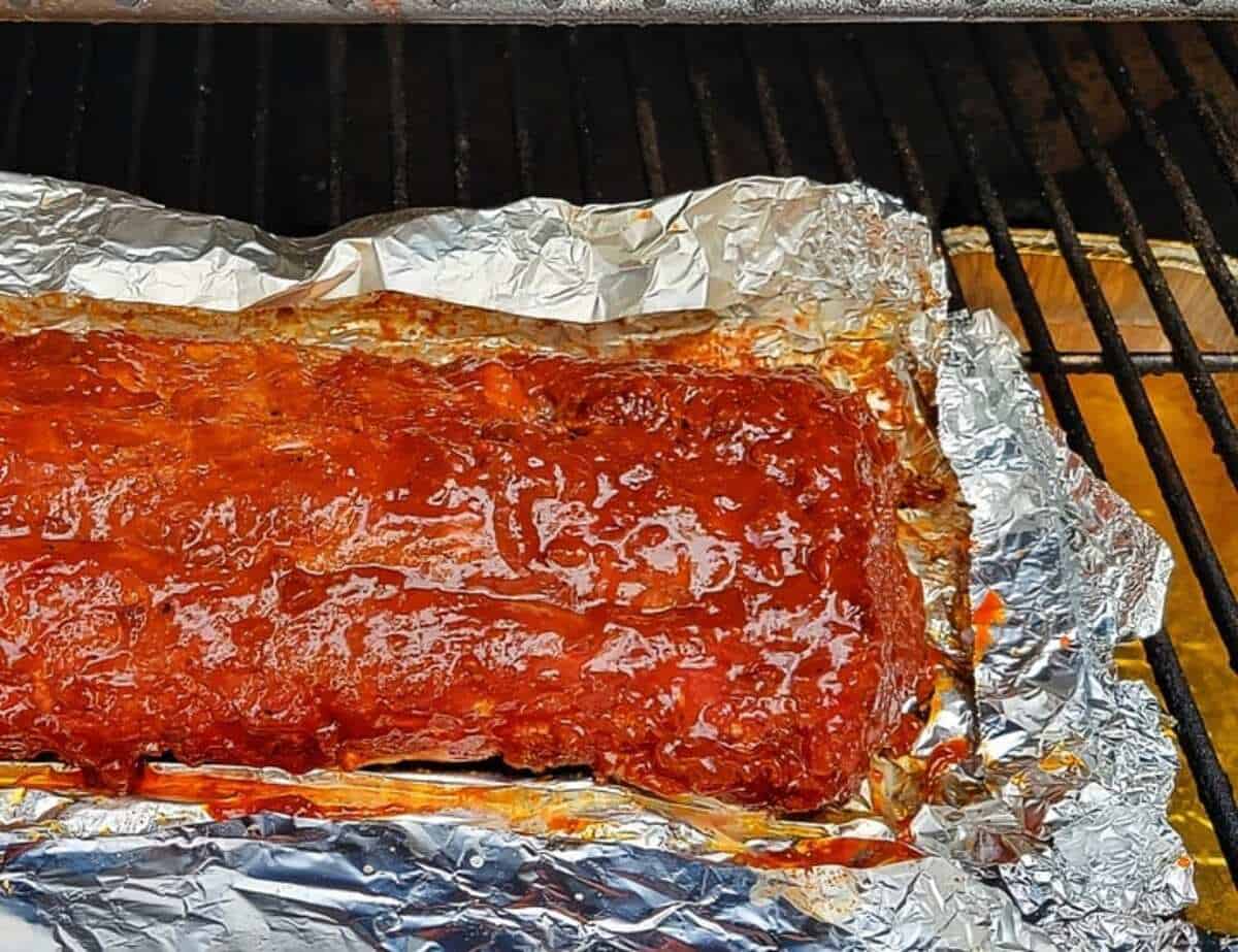 whole rack of ribs in opened foil on grill, covered in sauce