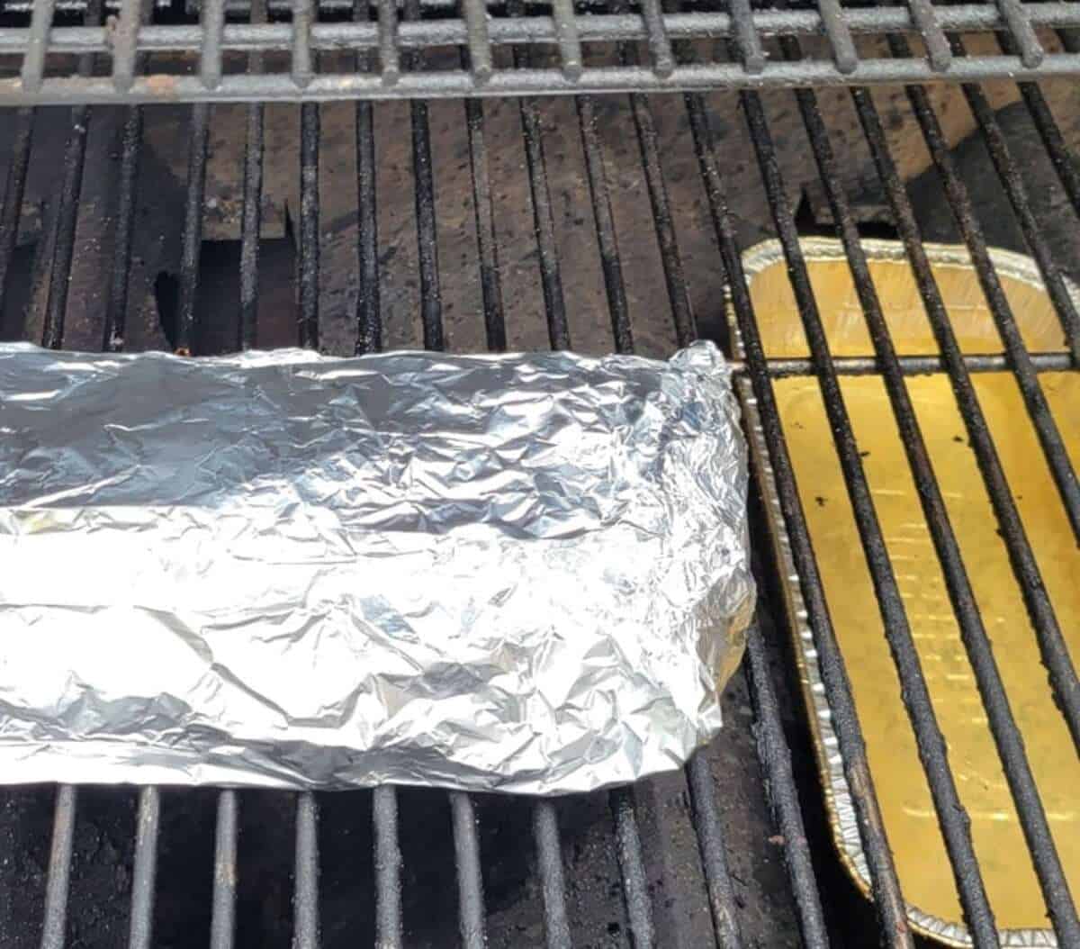 rack of ribs completely covered in foil on grill, foil water pan shown off to one side