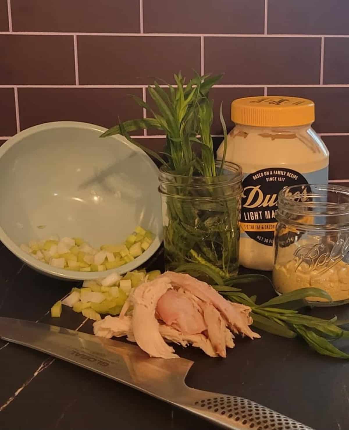 yellow onion and celery, fresh tarragon, jar of mayonnaise,, dijon mustard, chunks of roasted chicken, knife