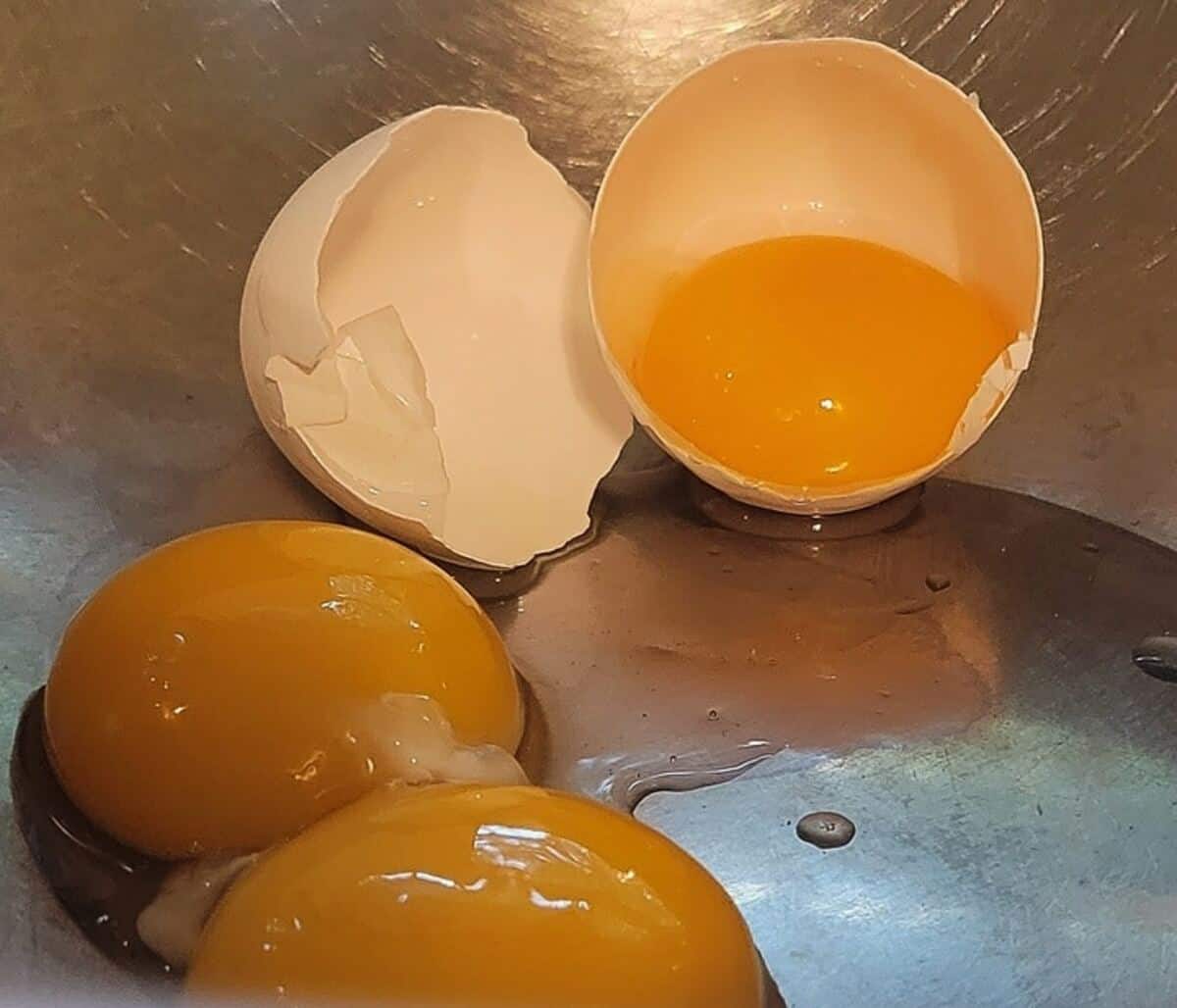 separated egg yolks in mixing bowl, one inside of shell cracked in half