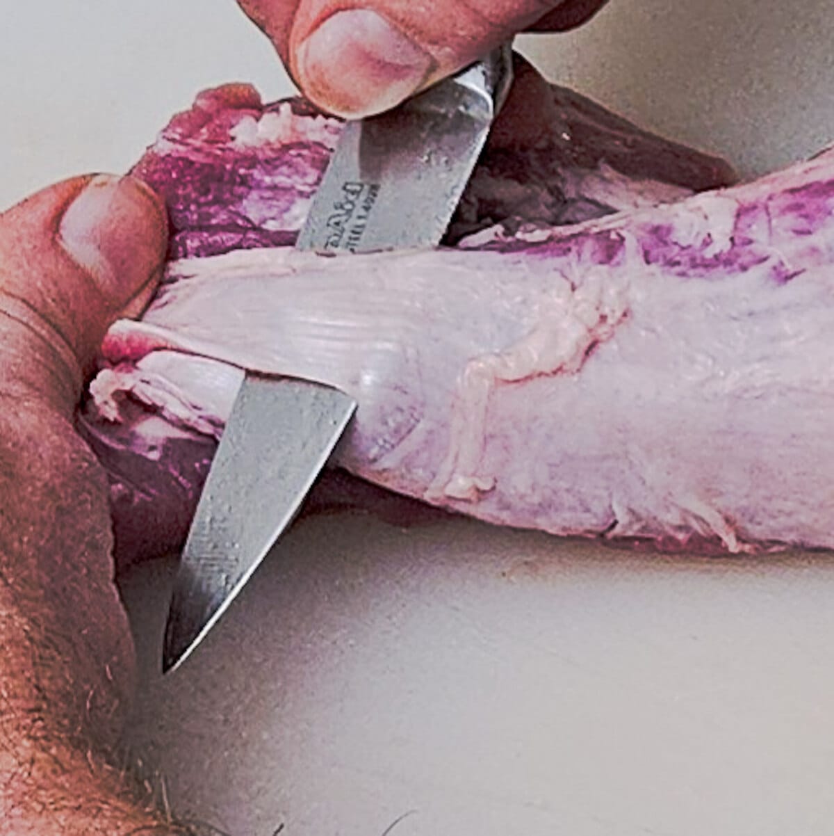 using a small knife to remove the silver skin from the pork tenderloin for the cast iron seared pork tenderloin with tangerine ginger sauce