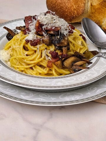 the finished pasta carbonara with mushrooms in a bowl served with extra cheese and bread close up image