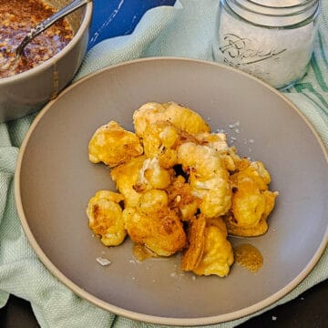 finished crispy cauliflower bites on a plate drizzled with spicy honey, and seasoned with flaky sea salt