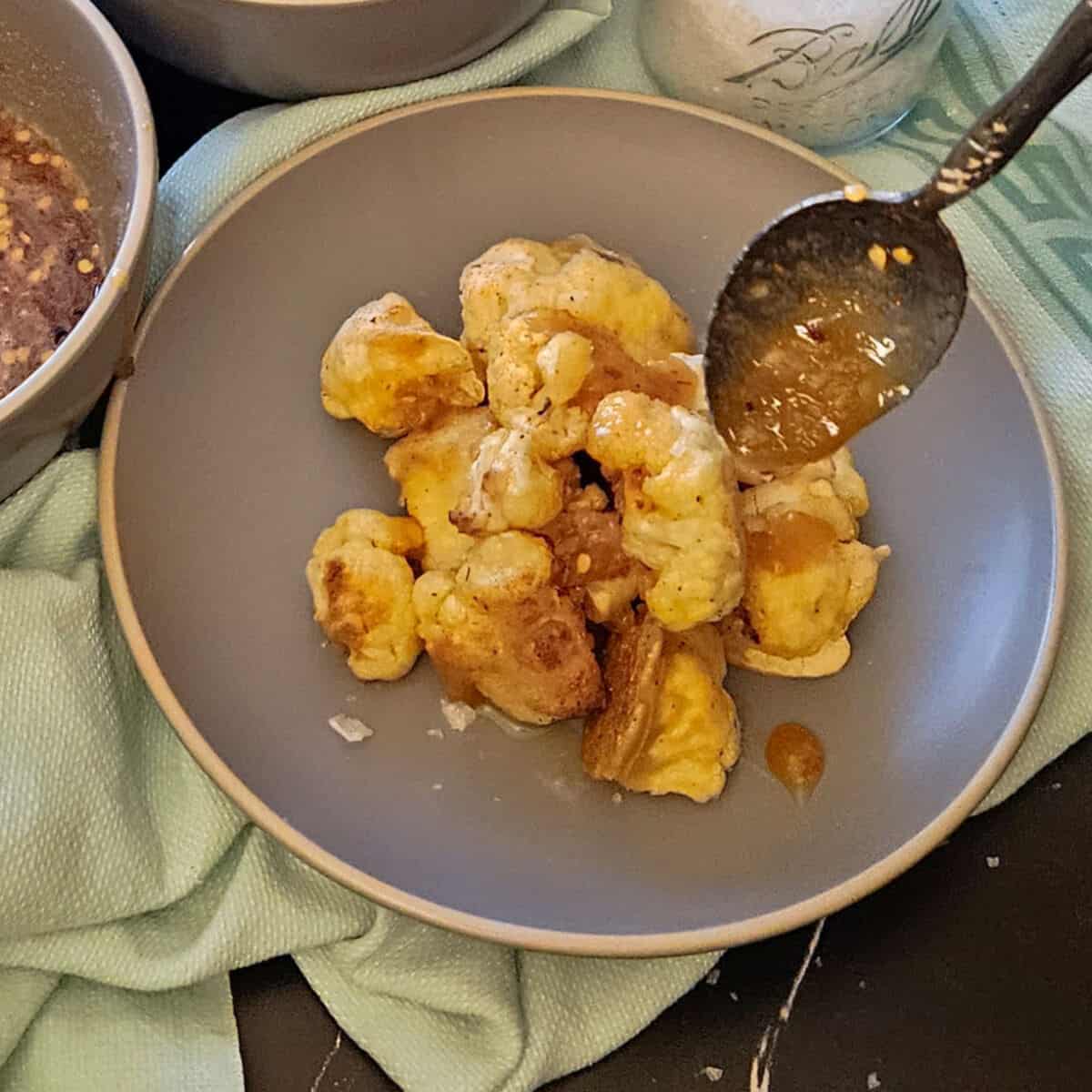 crispy cauliflower bites on a plate being drizzled with spicy honey