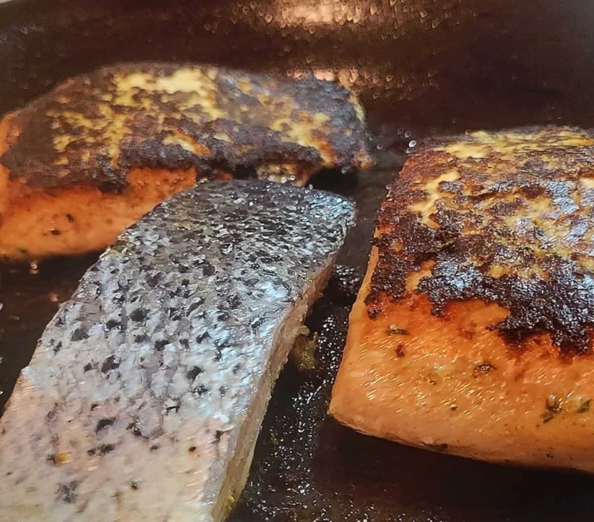 salmon shown in skillet being seared, seared side up and skin side up shown