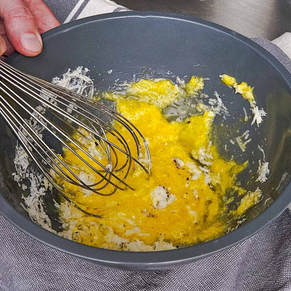 mixing together the eggs, grated cheese, and black pepper in a bowl using a wire whisk for the pasta carbonara with mushrooms