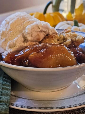 a serving of fresh peach cobbler in a bowl served with vanilla ice cream with pumpkins in the background