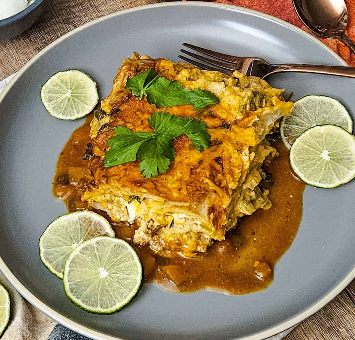 a serving of chicken enchilada casserole on a plate with fresh cilantro and sliced limes