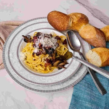 the over head image of the finished pasta carbonara with mushrooms in a bowl served with extra cheese and bread