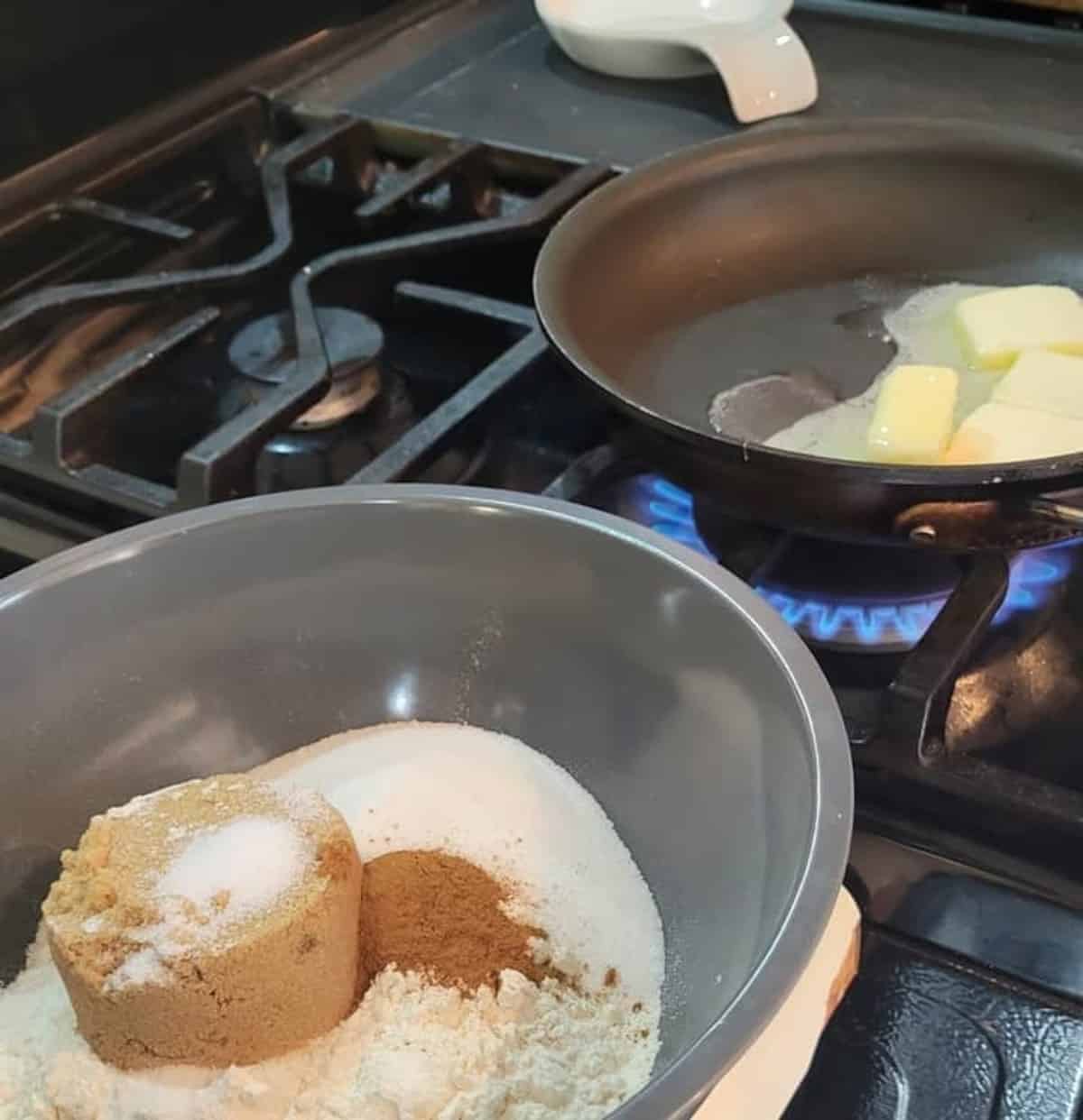 mixing bowl with dry ingredients un mixed shown in foreground, background showing a skillet over flame on stove, melting whole butter