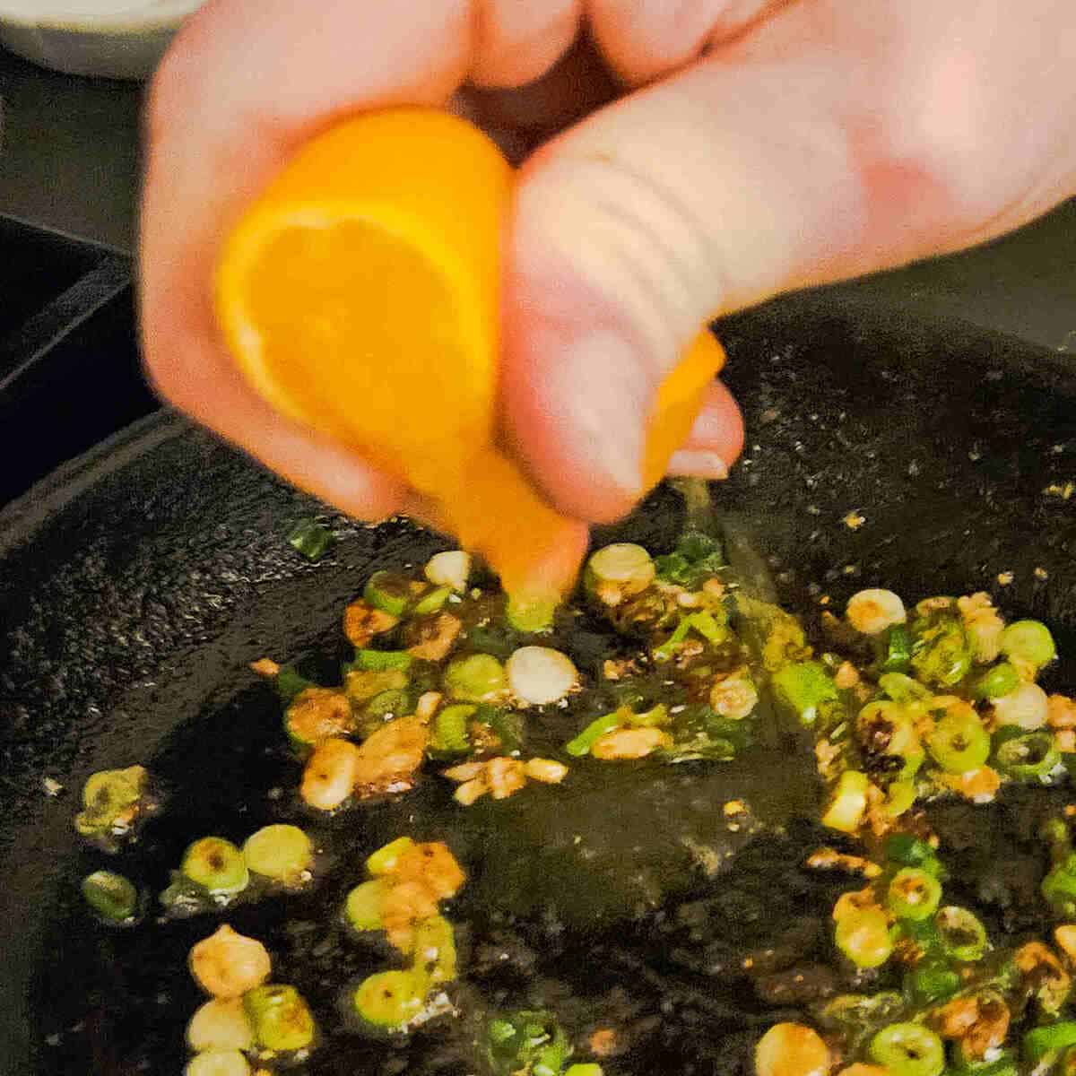a hand squeezing a fresh tangerine into a pan for the cast iron seared pork tenderloin with tangerine ginger sauce