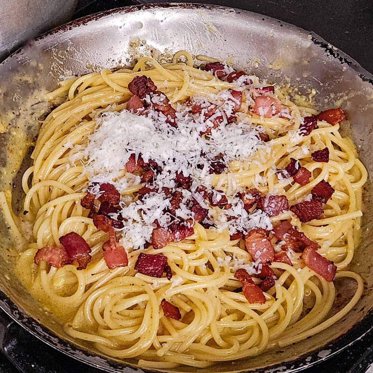 adding the cooked bacon pieces and cheese to the finished pasta in a pan for the pasta carbonara with mushrooms