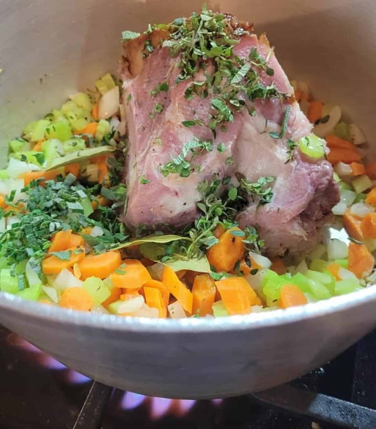 pot on stove over high heat, cut vegetables, ham bone, and herbs inside