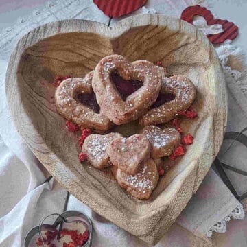 the finished best strawberry shortbread sandwich cookie recipe garnished with powdered sugar in a heart shaped wooden bowl