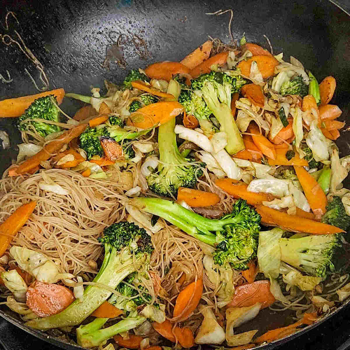 the cooked vegetables and rice noodles being tossed in the wok with soy sauce for the easy Asian vegetable stir fry rice noodles recipe