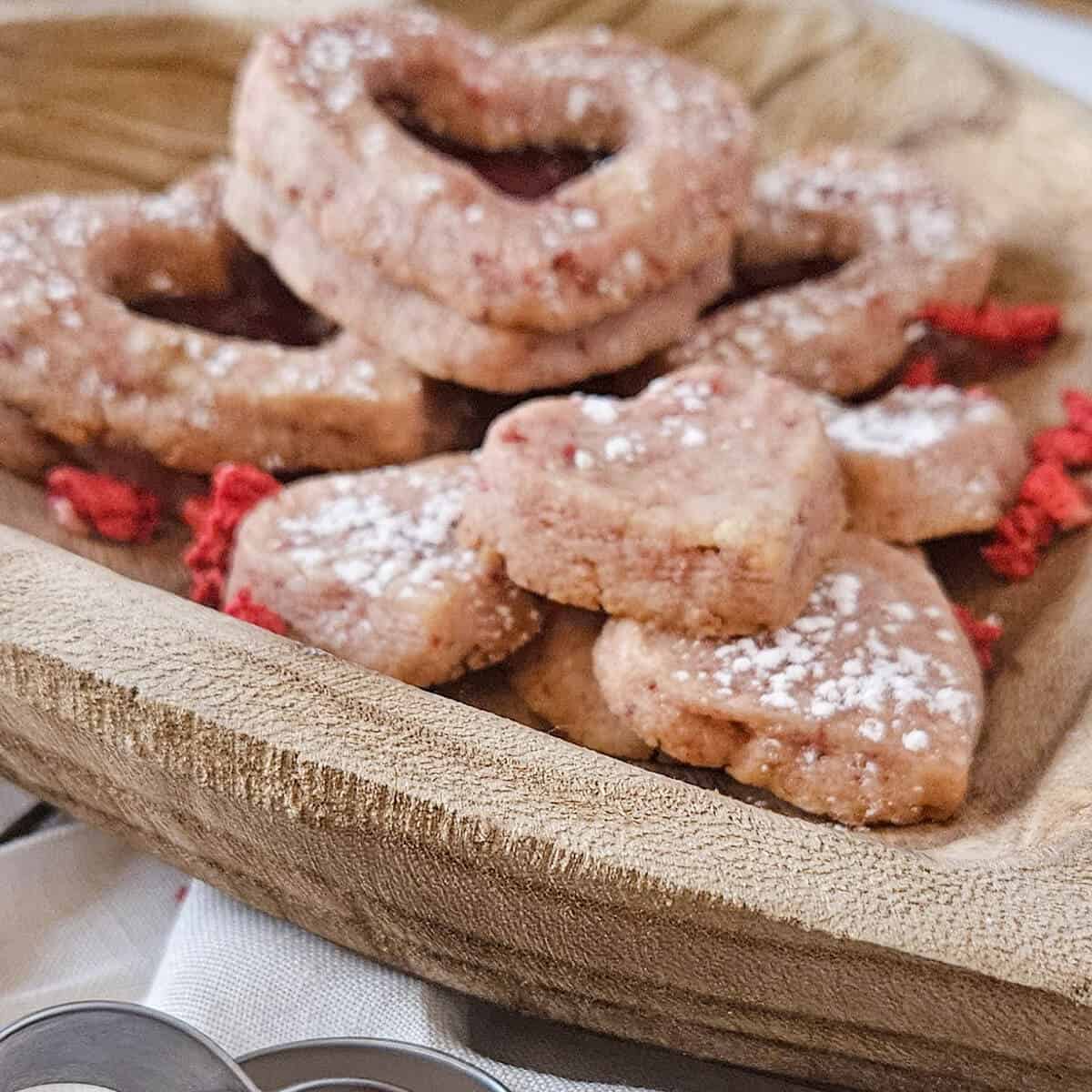 finished best strawberry shortbread sandwich cookies close up in a wooden heart shaped bowl, shaped like hearts