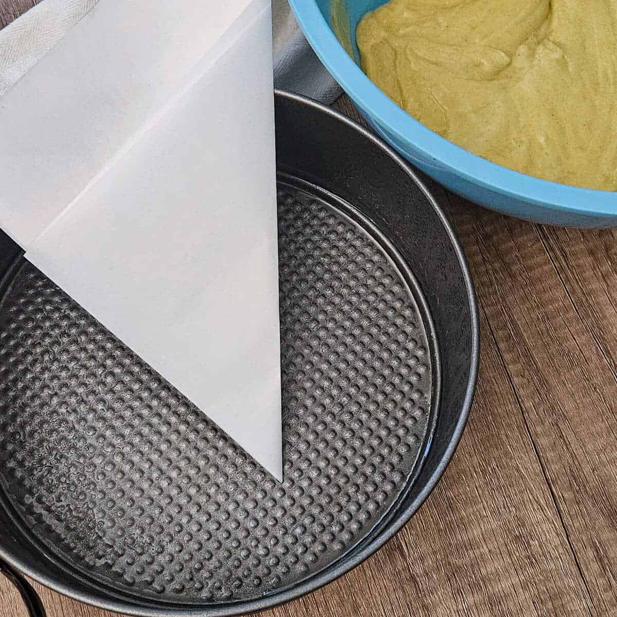 the batter for the gluten free olive oil cake in a bowl and the pan with the parchment paper folded and ready to cut to line the bottom of the pan