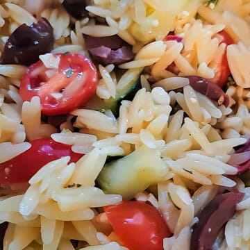 closeup image of finished Greek orzo pasta salad, including cherry tomatoes, Kalamata olives, and diced cucumber.