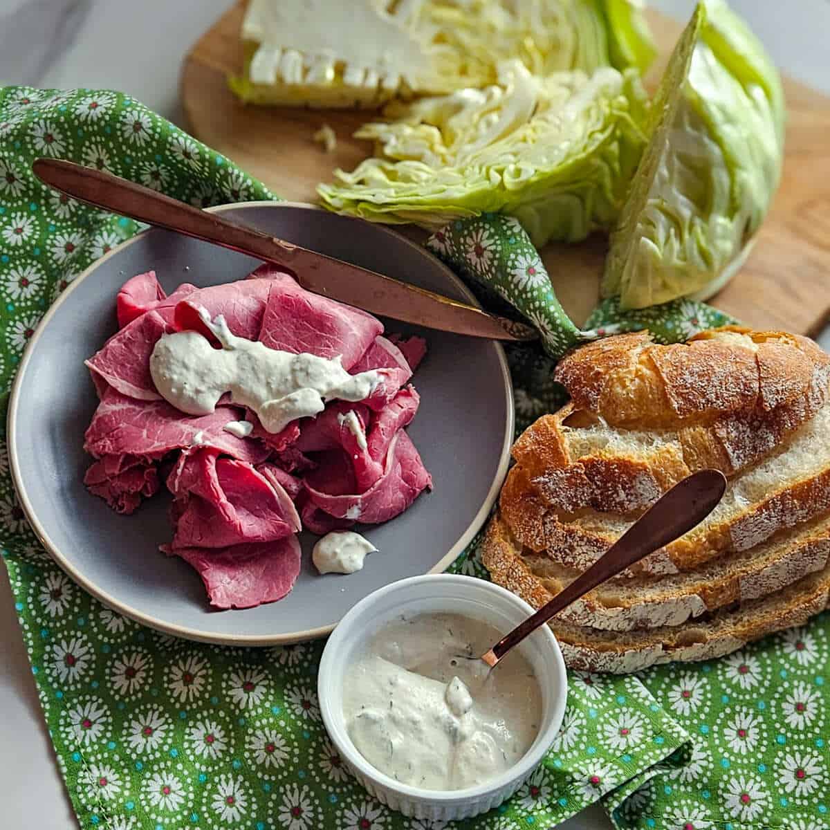 an image of corned beef on a plate with the best horseradish sauce on it, a small ramekin with the best creamy horseradish sauce, cut cabbage, and sliced bread