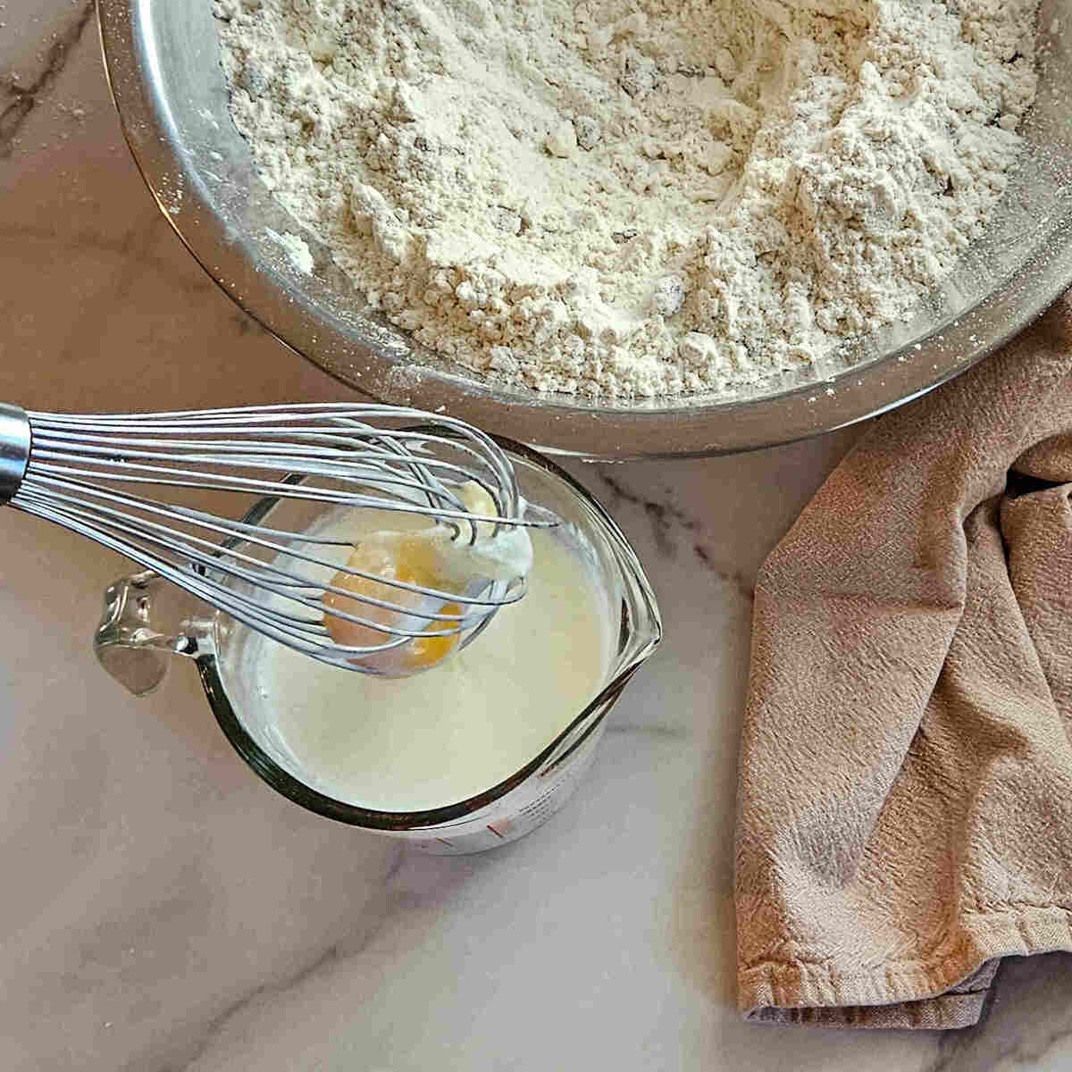 an image of the dry ingredients in a mixing bowl and the egg being whipped into the buttermilk with a wire whisk for the gluten free Irish soda bread