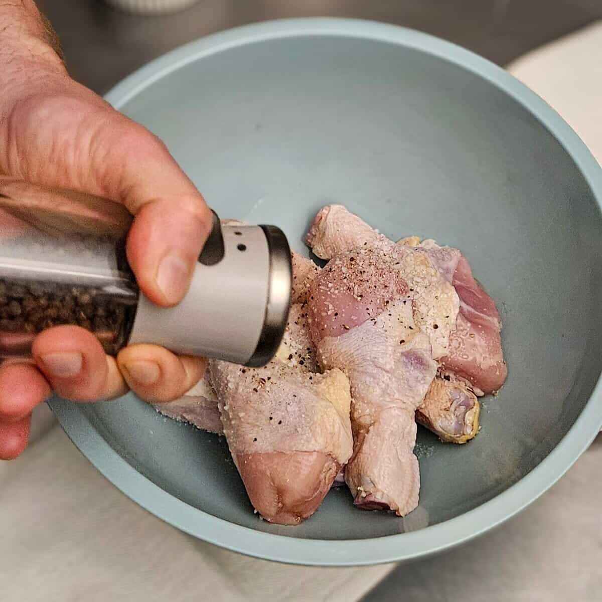 seasoning the raw chicken legs with black pepper for the chicken cottage pie recipe