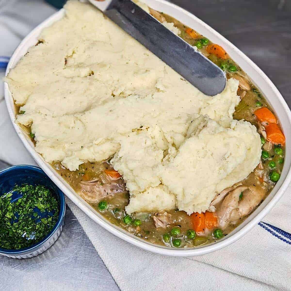 spreading the mashed potato topping onto the filling in a baking dish for the chicken cottage pie