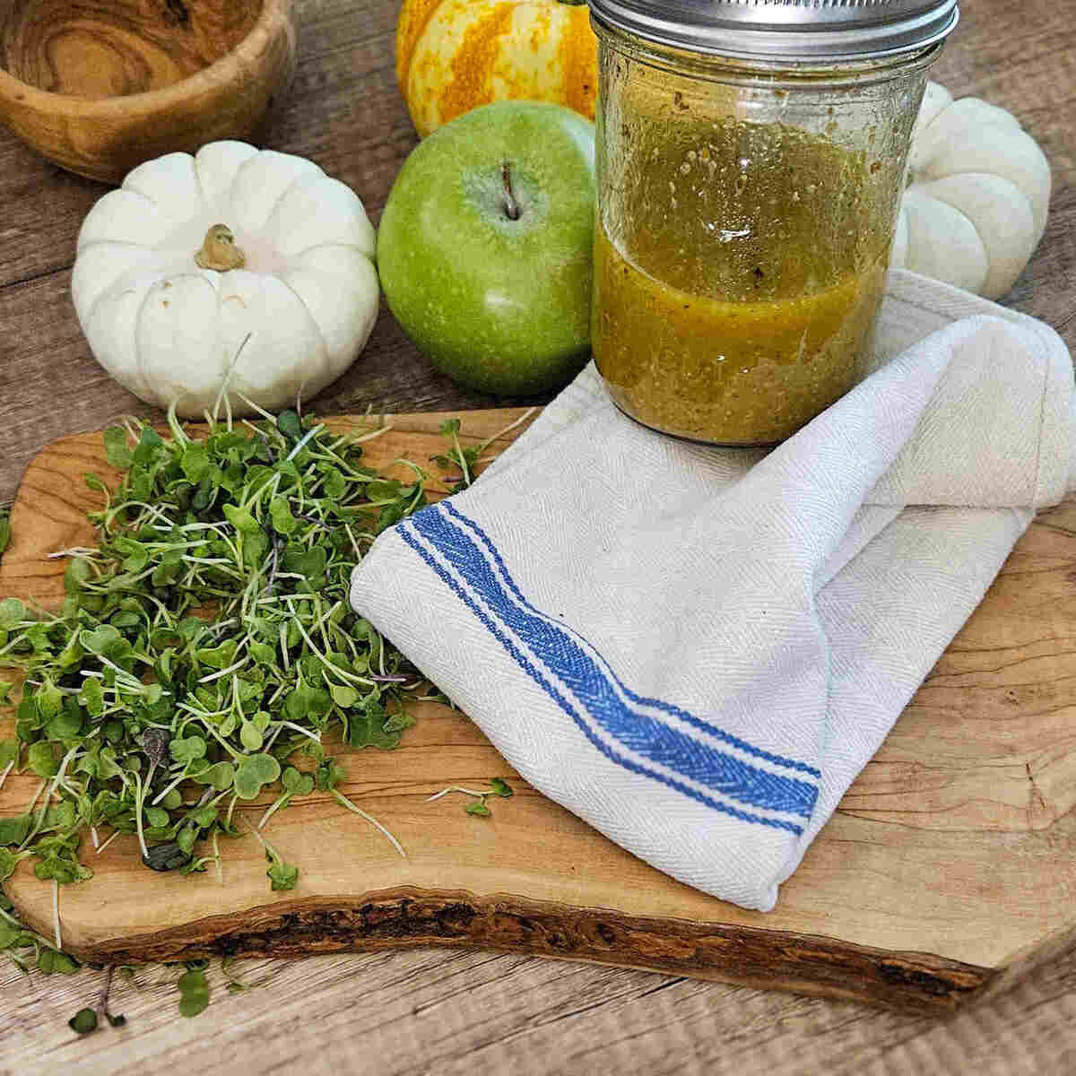 a mason jar full of vinaigrette with micro greens on a wooden cutting board and fall decorations.