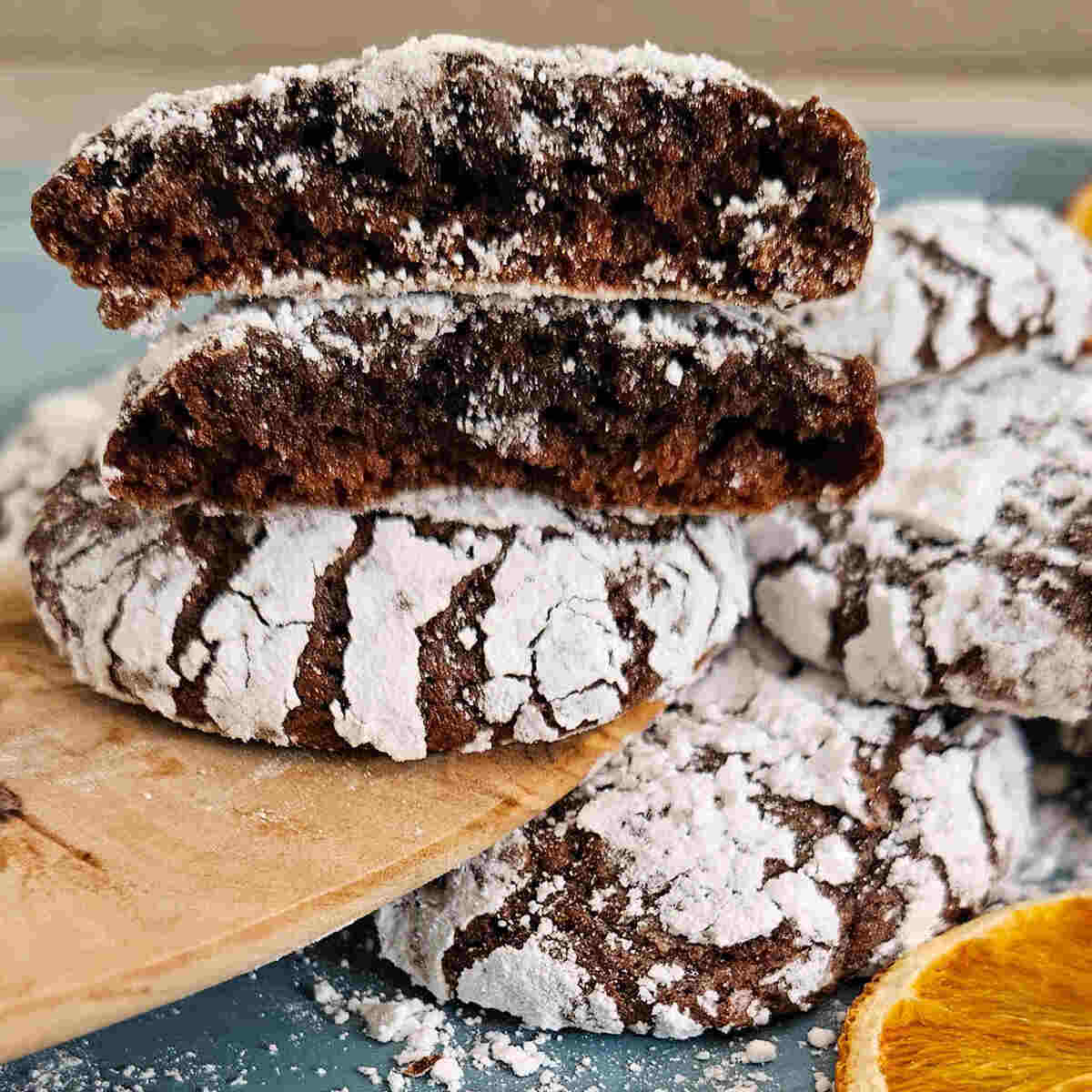 pile of dark chocolate pistachio crinkle cookies with one broken in half to show the soft interior