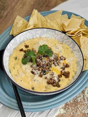 Queso Blanco dip with chorizo in a bowl garnished with cilantro leaves and cooked chorizo. Served with corn tortilla chips and a spoon.
