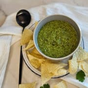 Homemade salsa verde in a bowl with a spoon, garnished with cilantro leaves and served with corn tortilla chips.