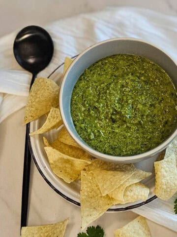 Homemade salsa verde in a bowl with a spoon, garnished with cilantro leaves and served with corn tortilla chips.