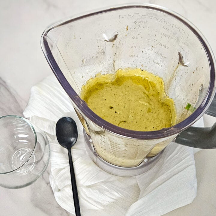 The pitcher of a blender with the charred lemon salad dressing blended and ready to place into a glass jar with a spoon.