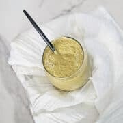 Charred lemon salad dressing in a glass jar with a spoon on a dish towel.