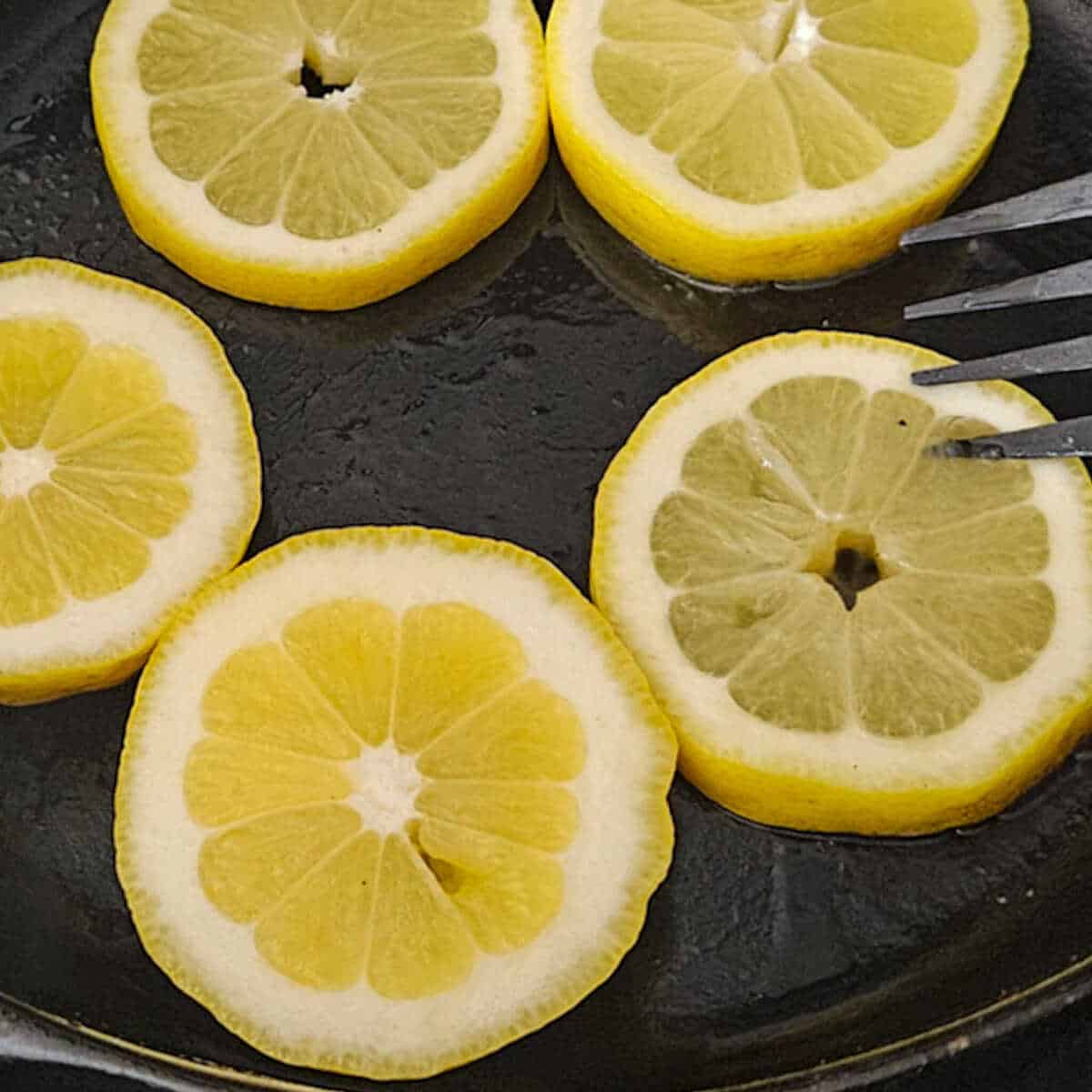 Adding the fresh lemon slices to a hot cast iron skillet for the charred lemon salad dressing recipe.