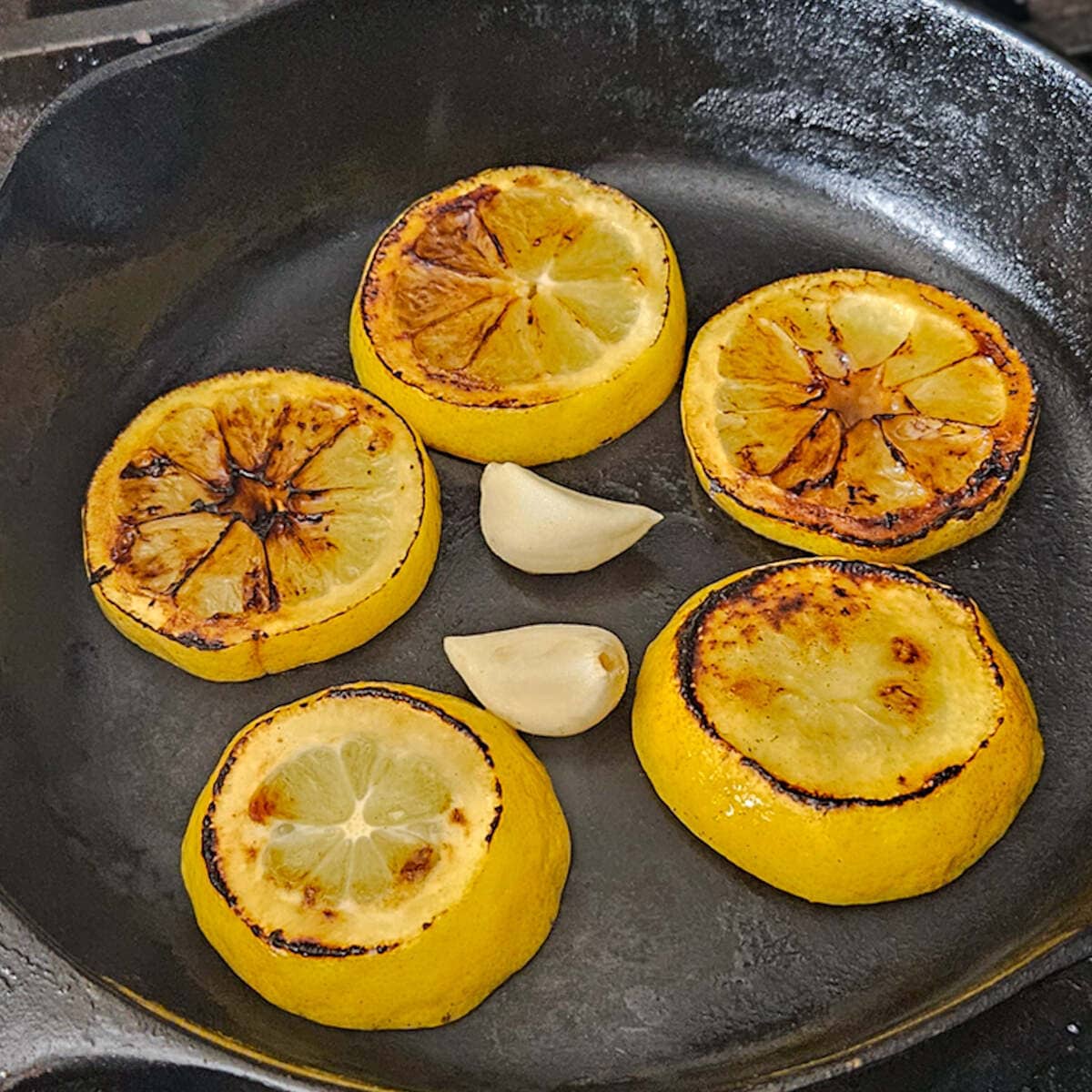 Charred lemon slices and garlic cloves in a cast iron skillet for the charred lemon salad dressing recipe.