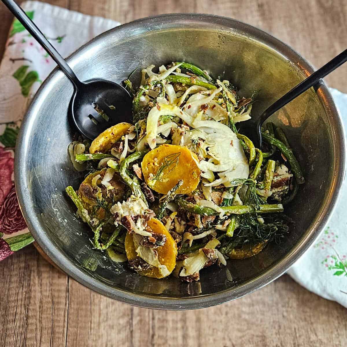 The ingredients for roasted asparagus and fennel salad with golden beets in a bowl tossed together with serving utensils.